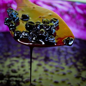 Chokeberry berries on a wooden cooking spoon over a pot full of chokeberry jam. Zavidovici, Bosnia and Herzegovina.