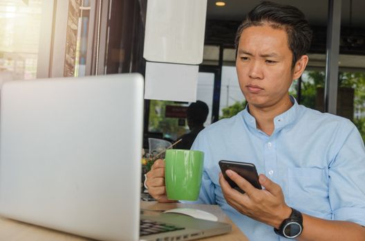 Asian businessmen are holding a cell phone, looking at data at the computer and worrying about work.