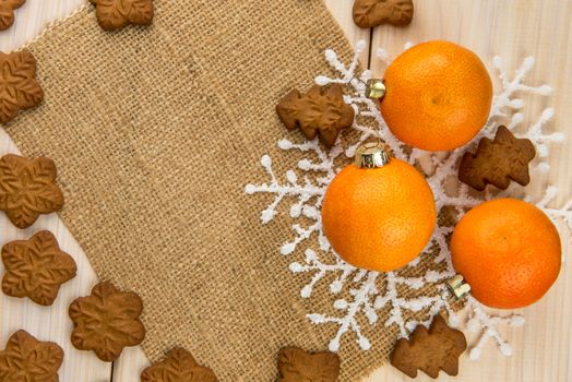 Christmas or New Year tangerines and gingerbread cookies with snowflakes framed on wooden background with brown sack background texture for text and your design.