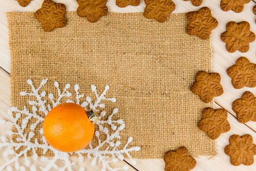 Christmas or New Year tangerines and gingerbread cookies with snowflakes framed on wooden background with brown sack background texture for text and your design.