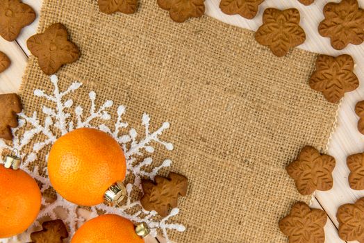 Christmas or New Year tangerines and gingerbread cookies with snowflakes framed on wooden background with brown sack background texture for text and your design.