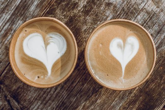 Two paper cups of coffee with heart shape latte art on wooden background on Valentine Day
