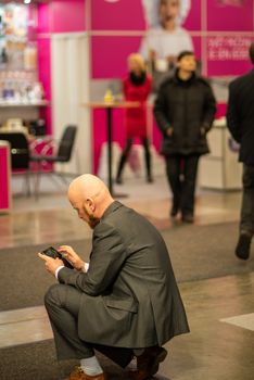 Young business (shaved head with bear) man checking his phone while attending an event at the convention trade center in Brno. BVV Brno Exhibition center. Czech Republic