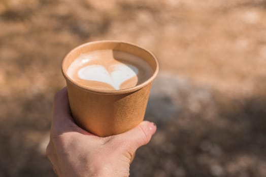Paper cup of coffee is holding on hand on nature background