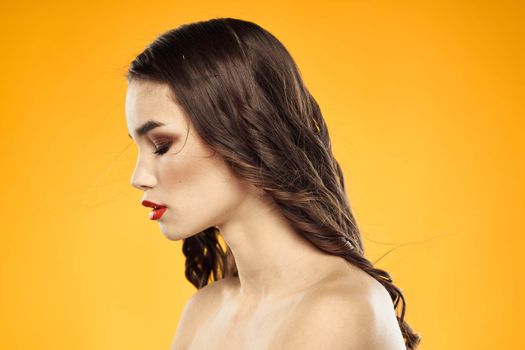 Beautiful brunette naked shoulders bright makeup red lips hairstyle close-up yellow background. High quality photo