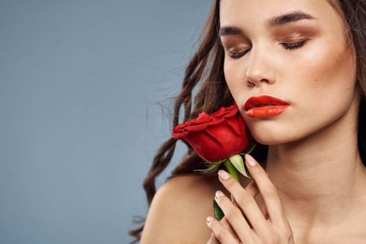 Woman portrait with red rose near the face on gray background and makeup curly hair. High quality photo