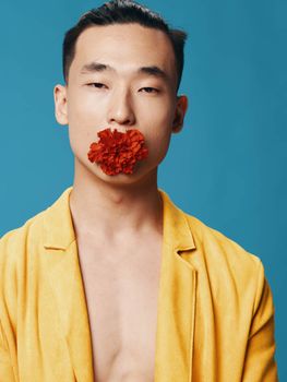 Asian man with a red flower in his teeth, yellow coat, naked torso. High quality photo