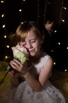 Cute lovely little girl with pink rose flower over dark background with garlands bokeh