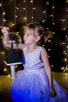 Cute little Child girl holding witch crystal ball with lightning and electricity over dark background with garlands bokeh