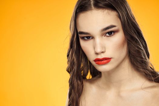 Beautiful brunette naked shoulders bright makeup red lips hairstyle close-up yellow background. High quality photo