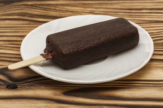 On a wooden table, on a saucer is ice cream in chocolate glaze on a stick