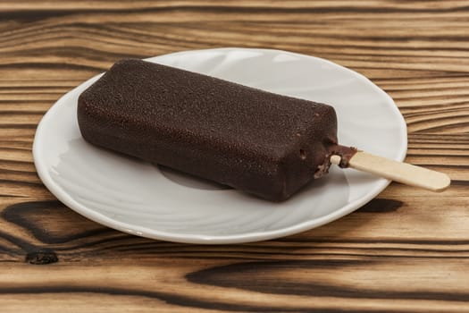 Ice cream in the chocolate glaze lies on a saucer on a wooden table
