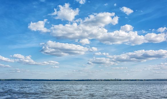 Against the background of the blue sky, over a large pond, cumulus clouds