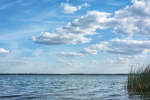 Cumulus clouds against the blue sky float above the surface of a large lake