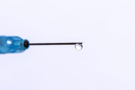 A transparent drop hangs on the tip of the medical needle