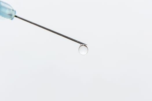 
A transparent drop hangs on the tip of the medical needle