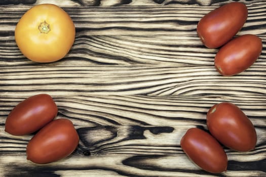 On the edges of the wooden surface are yellow and red tomatoes