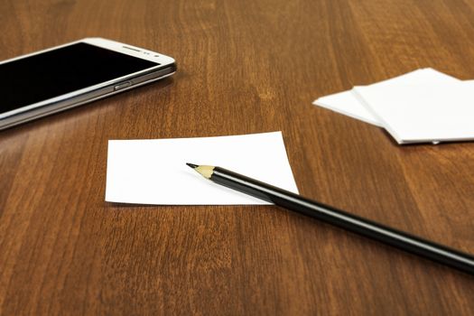 On the surface of the table is a smartphone and sheets for notes with a pencil