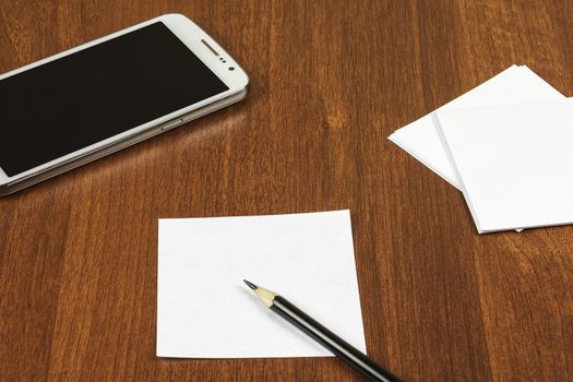 On the surface of the table lie a sheet for notes, a pencil and a smartphone