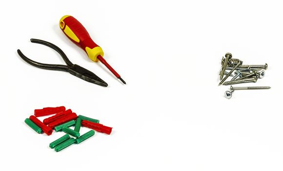 Screwdriver, pliers, screws and plastic dowels on a white background