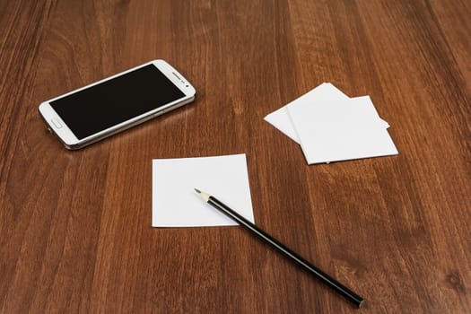 On the surface of the table is a smartphone, notes and a pencil