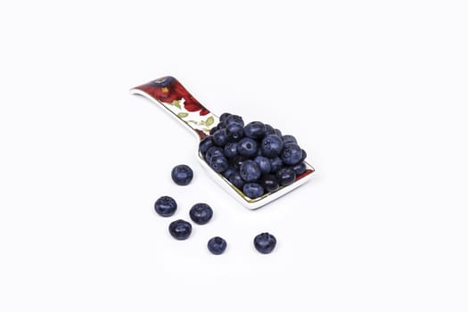 On a light background lies a porcelain spoon with large blueberry berries