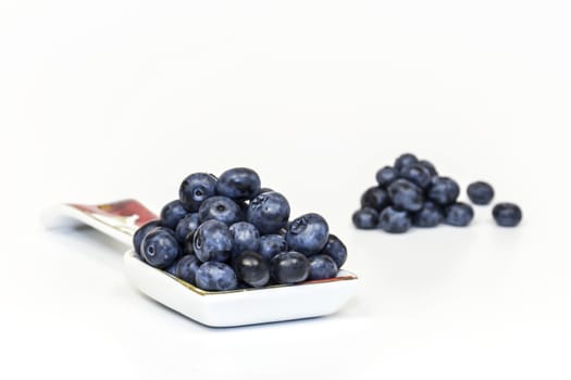 On a light background lie in a porcelain spoon lie large berries of blueberries