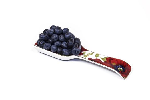 Large blueberries are in a spoon on a light background