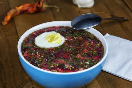 Cold soup with egg in a blue porcelain bowl is on a wooden table