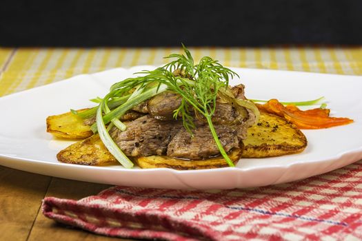 On a plate is roasted meat with potatoes, carrots and greens