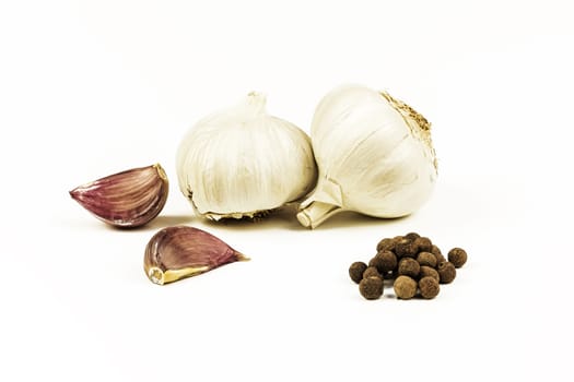 On a white background lie heads and uncooked cloves of garlic with peppercorns