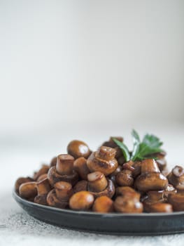 Ready-to-eat fried mini champignons on plate with copy space. Perfect mini mushrooms heap on plate over gray cement background. Natural day light. Vertical.