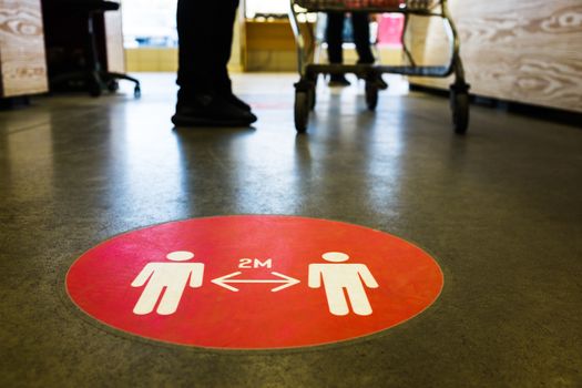 Red round sign printed on ground at supermarket cash desk register informing people to keep 2 meter 6 feet distance from each other,prevent spreading Coronavirus COVID-19 virus disease infection,UK&US
