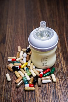 Small baby bottle, filled with milk, surrounded with natural supplement, against a wood background