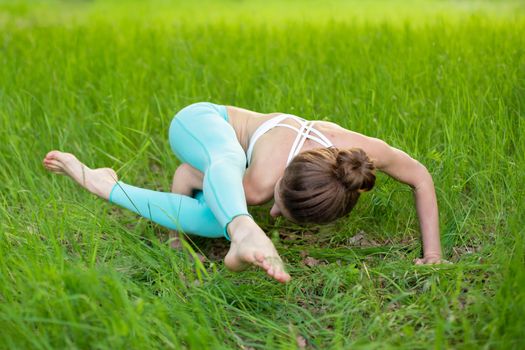 A young sports girl practices yoga in a quit green summer forest, yoga assans posture. Meditation and unity with nature.