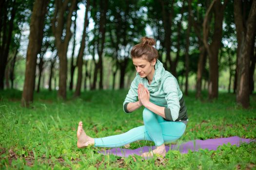 A young sports girl practices yoga in a quit green summer forest, yoga assans posture. Meditation and unity with nature.