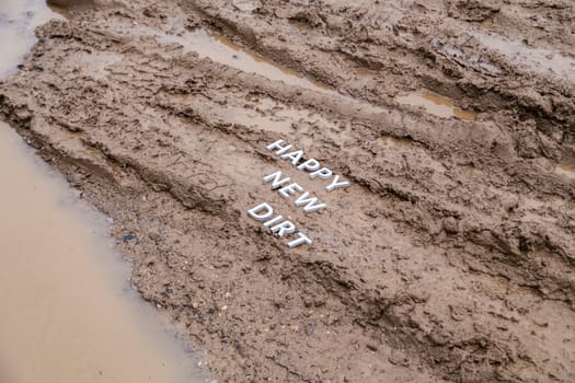 the words happy new dirt laid with silver metal letters on wet mud surface in diagonal perspective under cloudy autumn day light