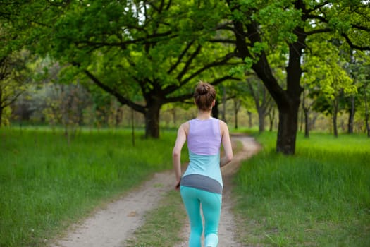 Sports brunette girl jogging in the park. Green forest on the background.