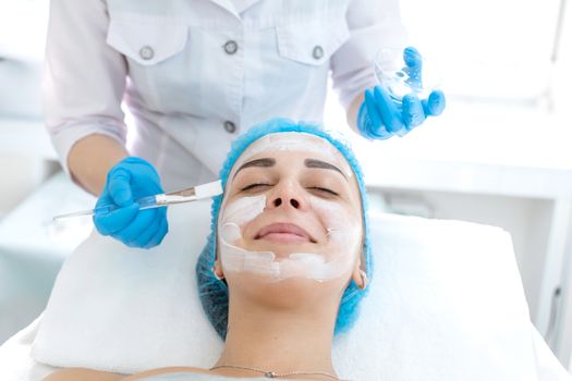 Woman professional doctor beautician applies a mask on a patient's face for skin care. Cosmetic procedures for skin rejuvenation and nutrition.