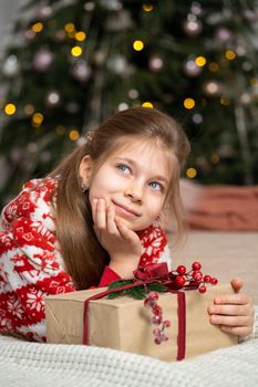 A little girl in pajamas early in the morning found a present from Santa under the tree. Christmas magic fairy tale. Happy childhood.