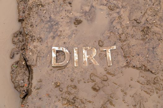 the word mud imprinted in wet dirt road surface and puddle - close-up with selective focus in flat lay perspective.
