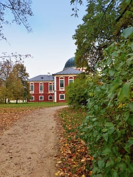 A view of part of beautiful baroque Veltrusy state castle through leaves of bush and path in autumn season.