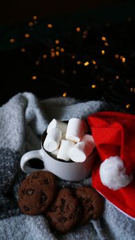 Mug of hot chocolate with christmas hat, marshmallow and chocolate cookies. Christmas spirit, hot winter drink. Selective focus - vertical photo