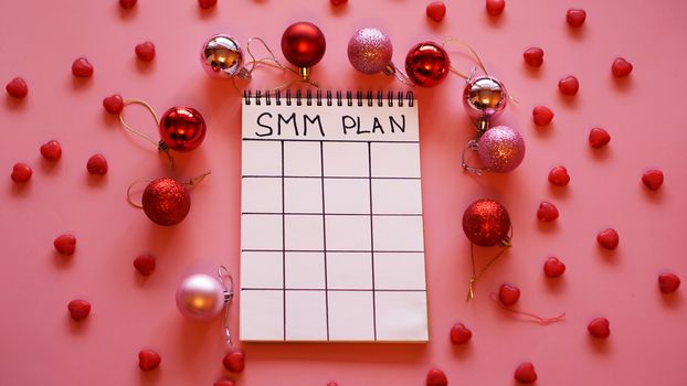 Freelance project. SMM plan blank. White sheet on a pink festive background with red Christmas balls and candy in the form of hearts
