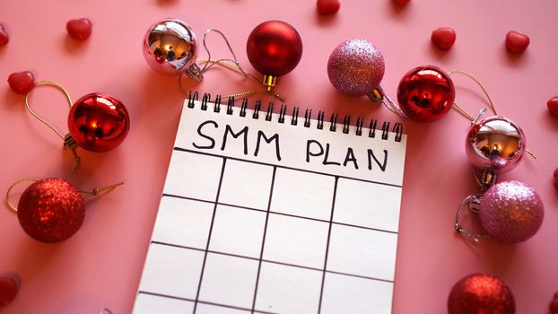 Freelance project. SMM plan blank. White sheet on a pink festive background with red Christmas balls and candy in the form of hearts