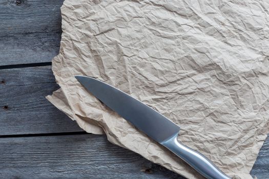sharp knife on crumpled craft paper on wooden background, copy space.