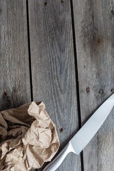 sharp knife on crumpled craft paper on wooden background, copy space.