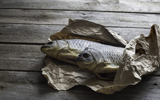 Salted Dry fish vobla on crumpled craft paper on wooden background, delicious beer snack, close-up.