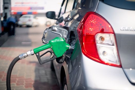 Man at a petrol pump fuel station inserting nozzle into fuel tank of a car and starting the fuel pumping in the auto cut off petro diesel pump. Shows the high dependence of india on fossil unleaded fuels shown by the green nozzle as this non renewable environment friendly fuel is replaced by cheaper alternatives