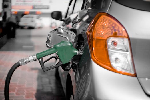 Man at a petrol pump fuel station inserting nozzle into fuel tank of a car and starting the fuel pumping in the auto cut off petro diesel pump. Shows the high dependence of india on fossil unleaded fuels shown by the green nozzle as this non renewable environment friendly fuel is replaced by cheaper alternatives